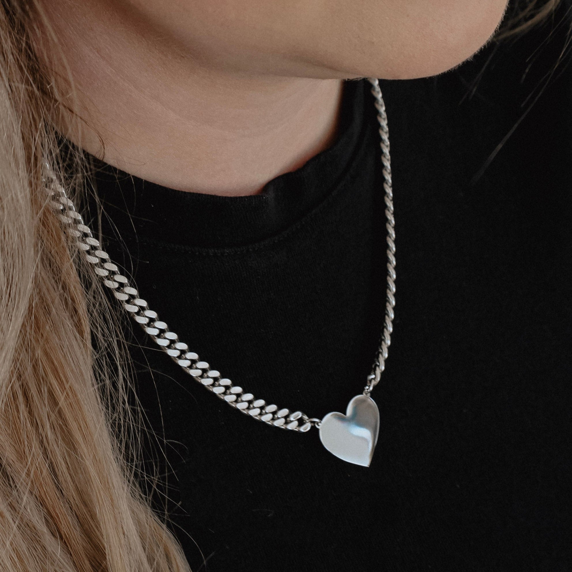 Silver chain necklace with a heart pendant worn by a person against a black background